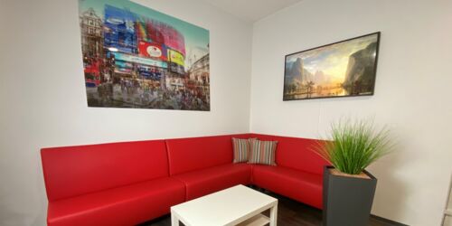 Wartebereich der Rezeption von MEDANDSPORTS mit roter Ledereckcouch und Tisch
